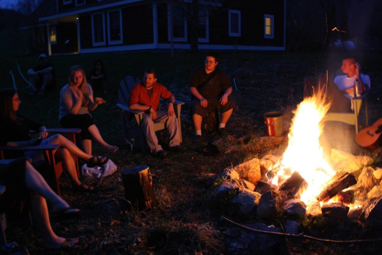 group of people sitting around bonfire at night