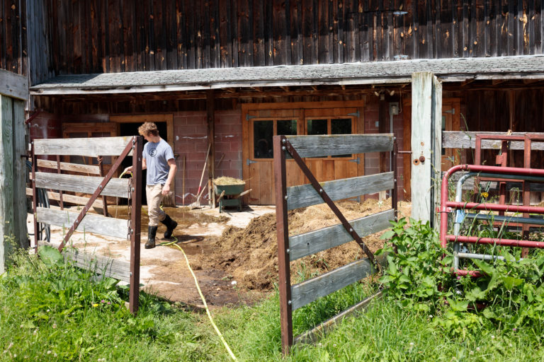 man cleaning outside barn with hose