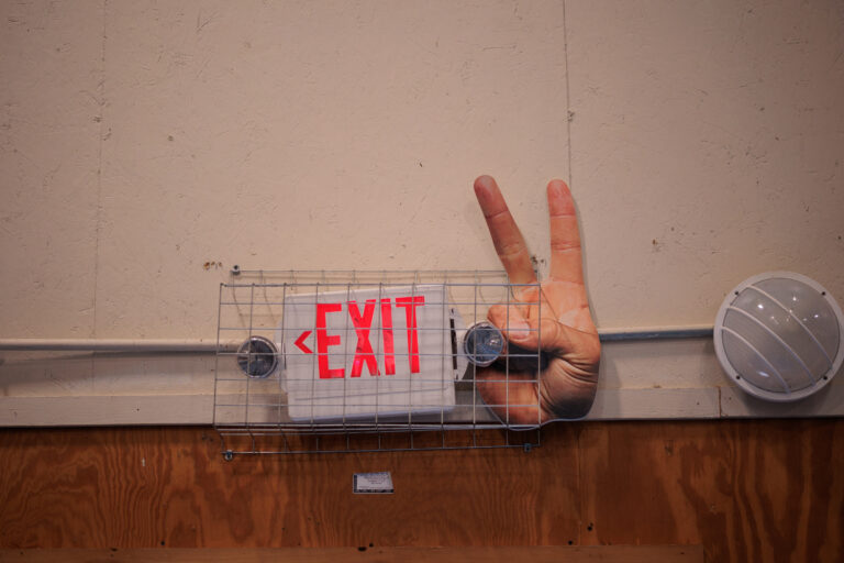 A picture of a hand making a peace sign next to a red exit light
